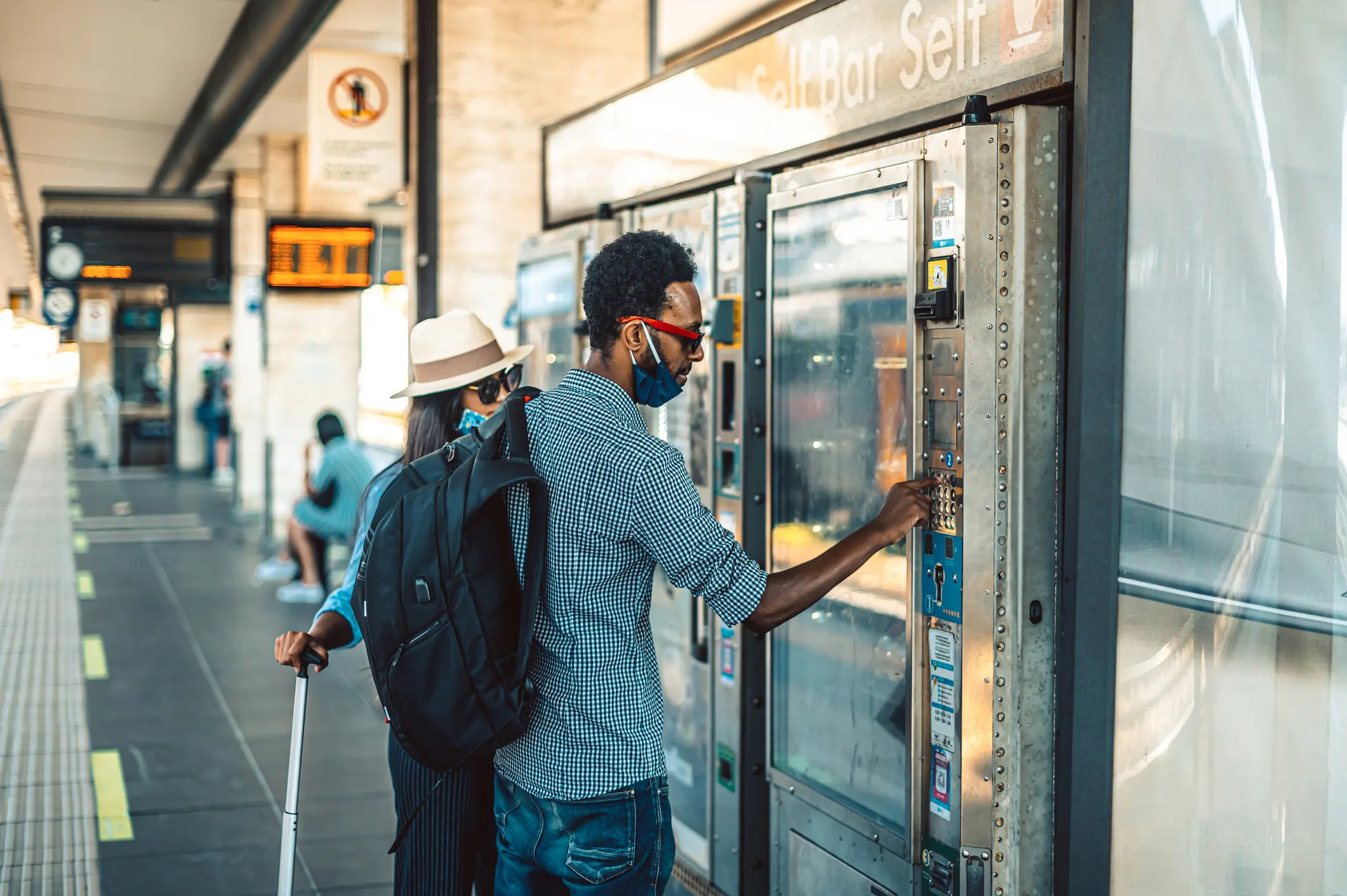 A man in a mask selects a drink from a vending machine.
