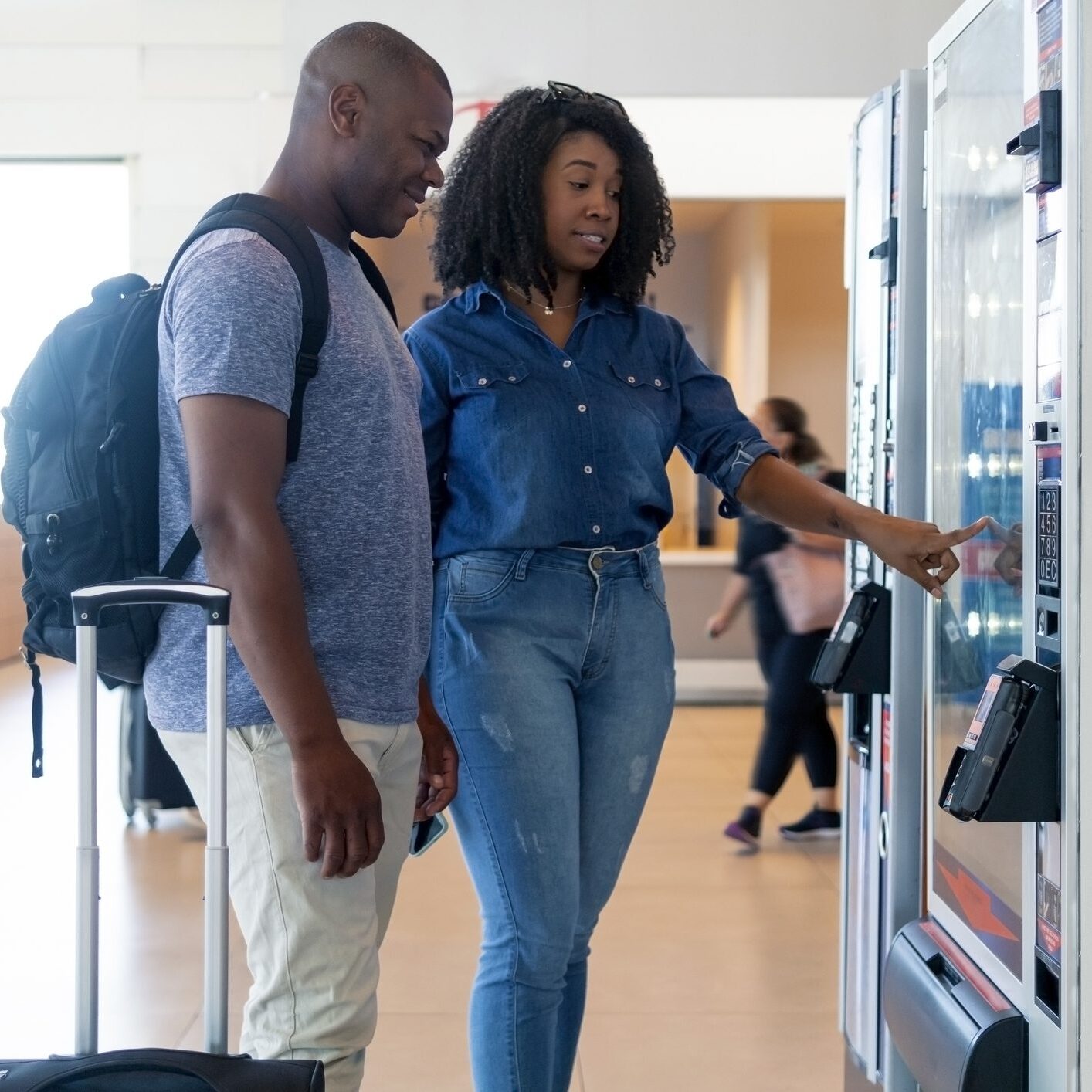 Two people choosing snacks from a vending machine.